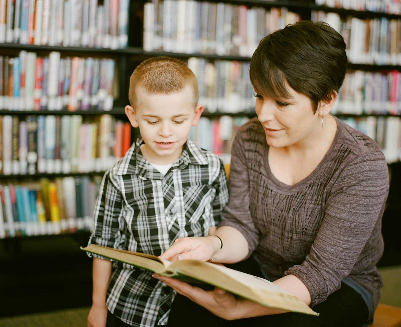 A tutor reading through a book with a young student in a library